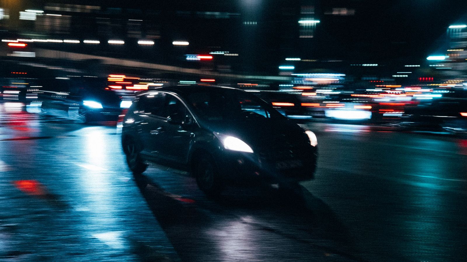 רכב נוסע ברחוב עירוני רטוב בלילה עם אורות מטושטשים